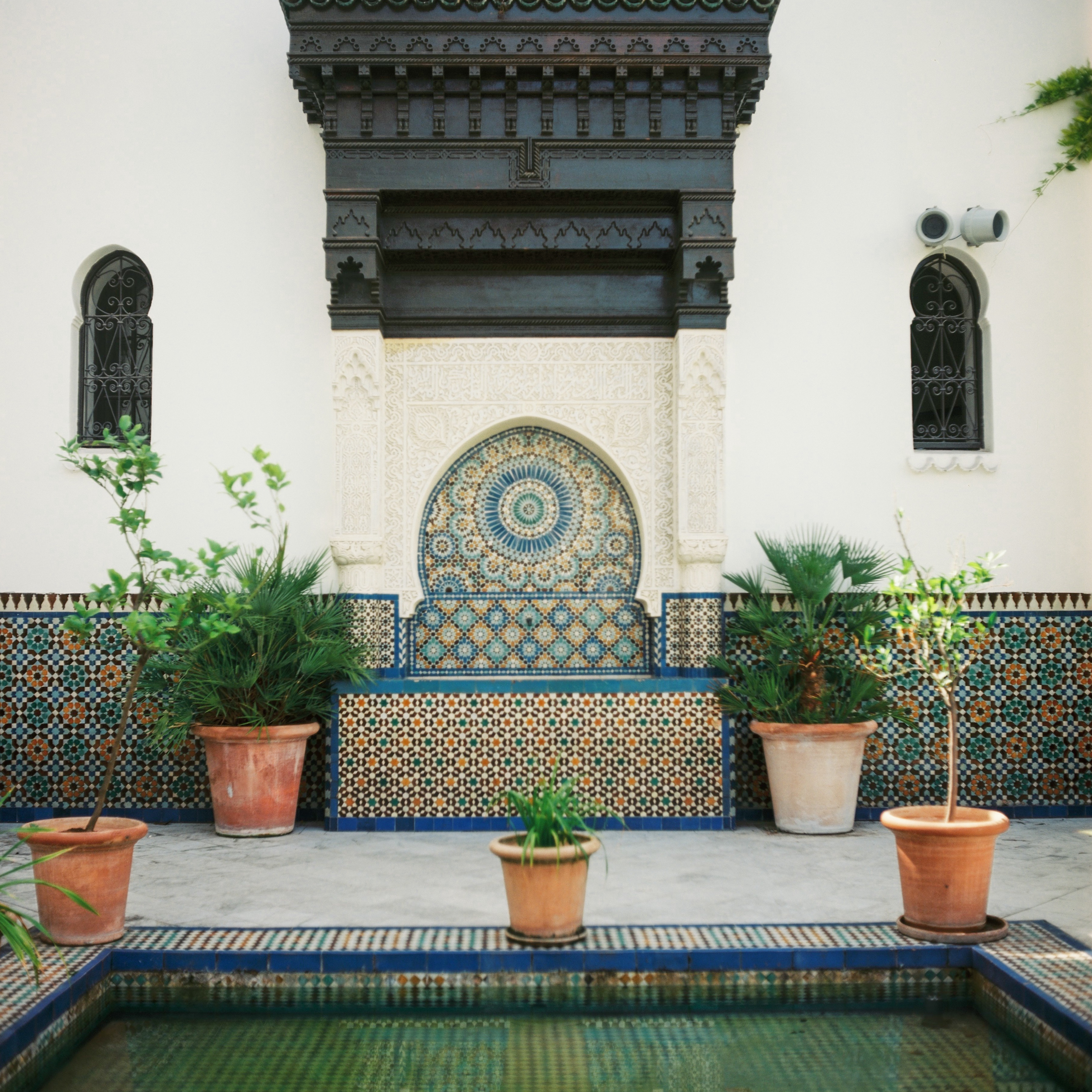 intricate blue and yellow tile mosaics next to a small pool at la grande mosquée de paris
