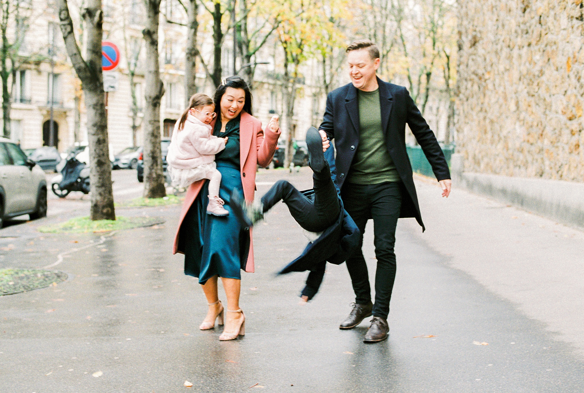 Two parents swinging their son by the arms on the sidewalk in Paris