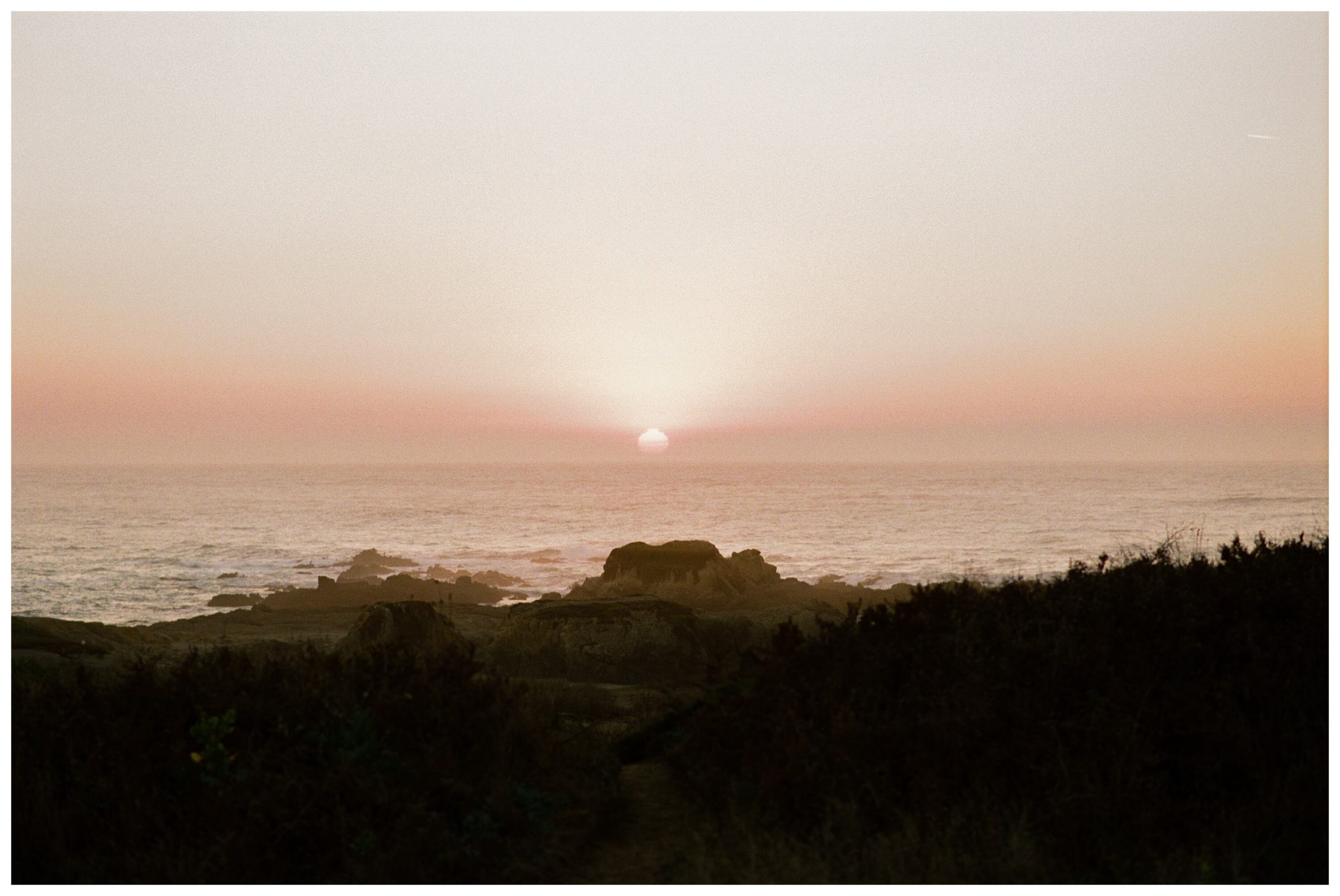 A sunset on Glass Beach in Fort Bragg, a northern California coastal town. The sky is hazy orange and red, making the sun appear exceptionally large.