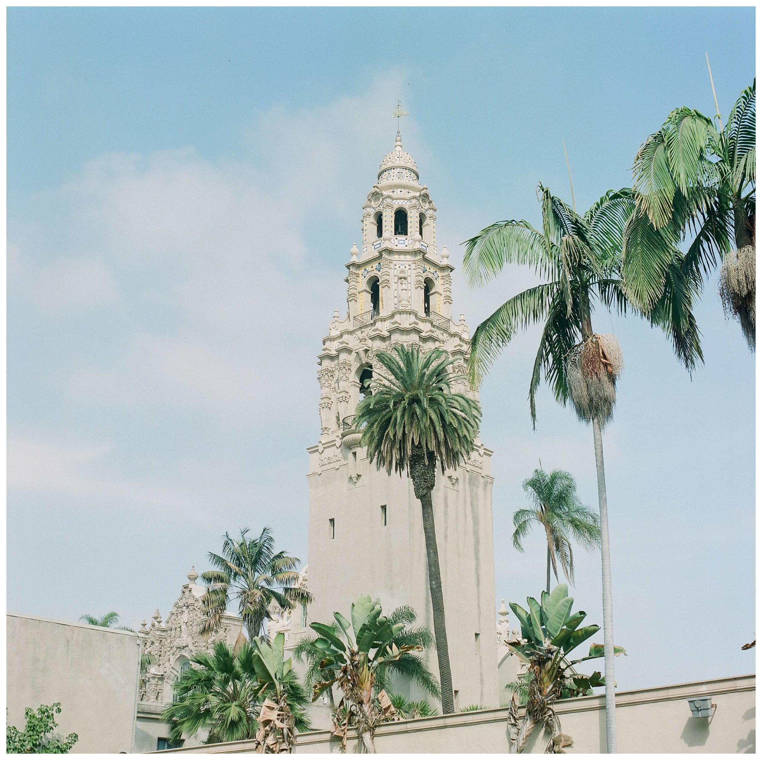 The California Tower, a mix of Plateresque, Baroque, Churrigueresque, and Rococo, Gothic, and Spanish-Colonial styles, rises against the bright blue sky with the palm trees on a sunny day at Balboa Park.