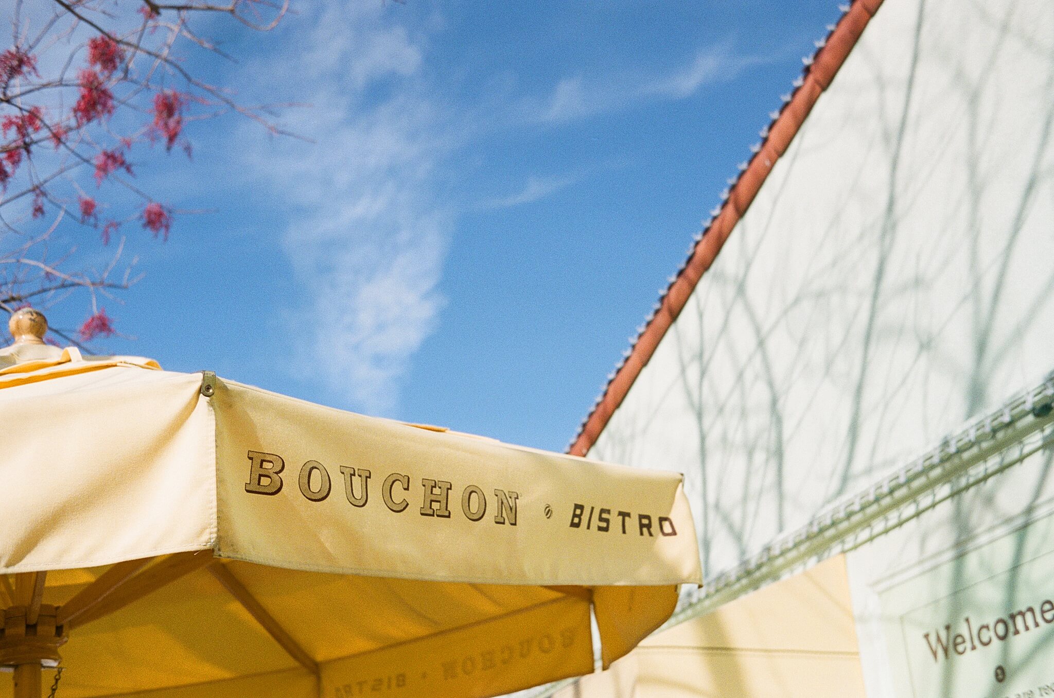 roller 35 sample image. A sunny yellow patio umbrella with the words "bouchon bistro" emblazoned across a flap contrasts with the clear blue sky.