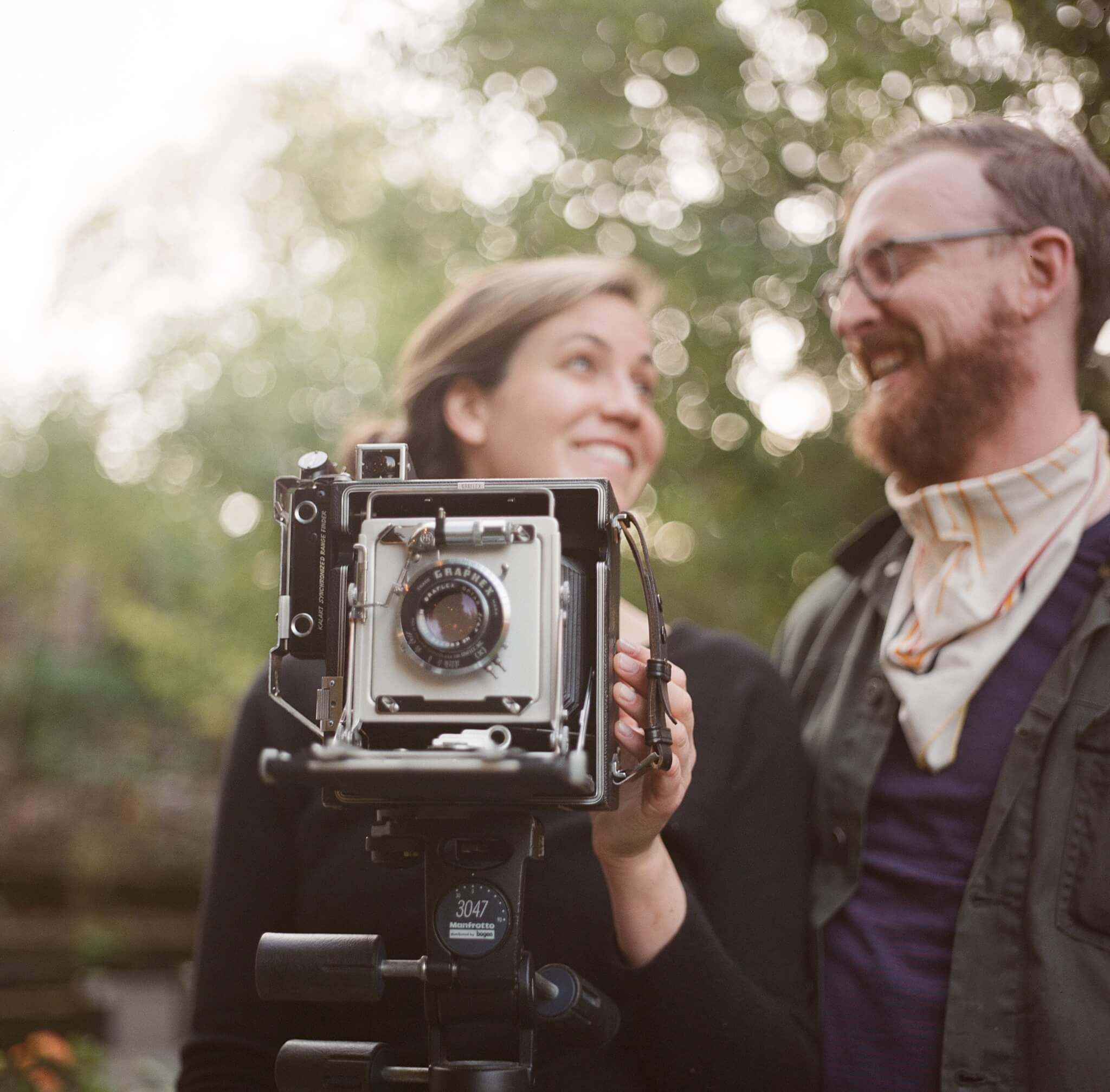 hasselblad 500 cm review and sample image on portra 160. A couple laughs and smiles at each other behind a Speed Graphic 4x5 camera.