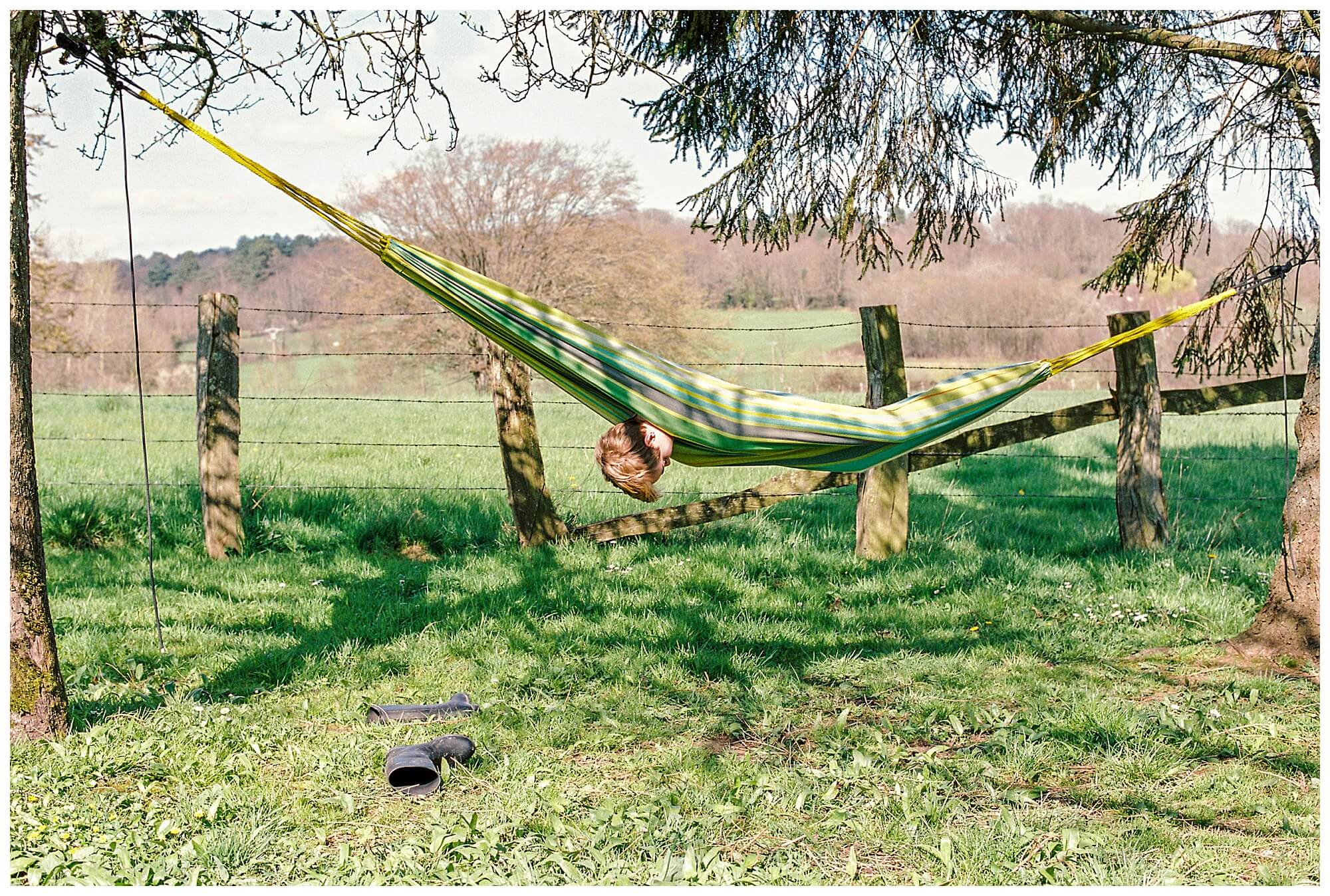 A young French boy hangs upside-down in a hammock. 