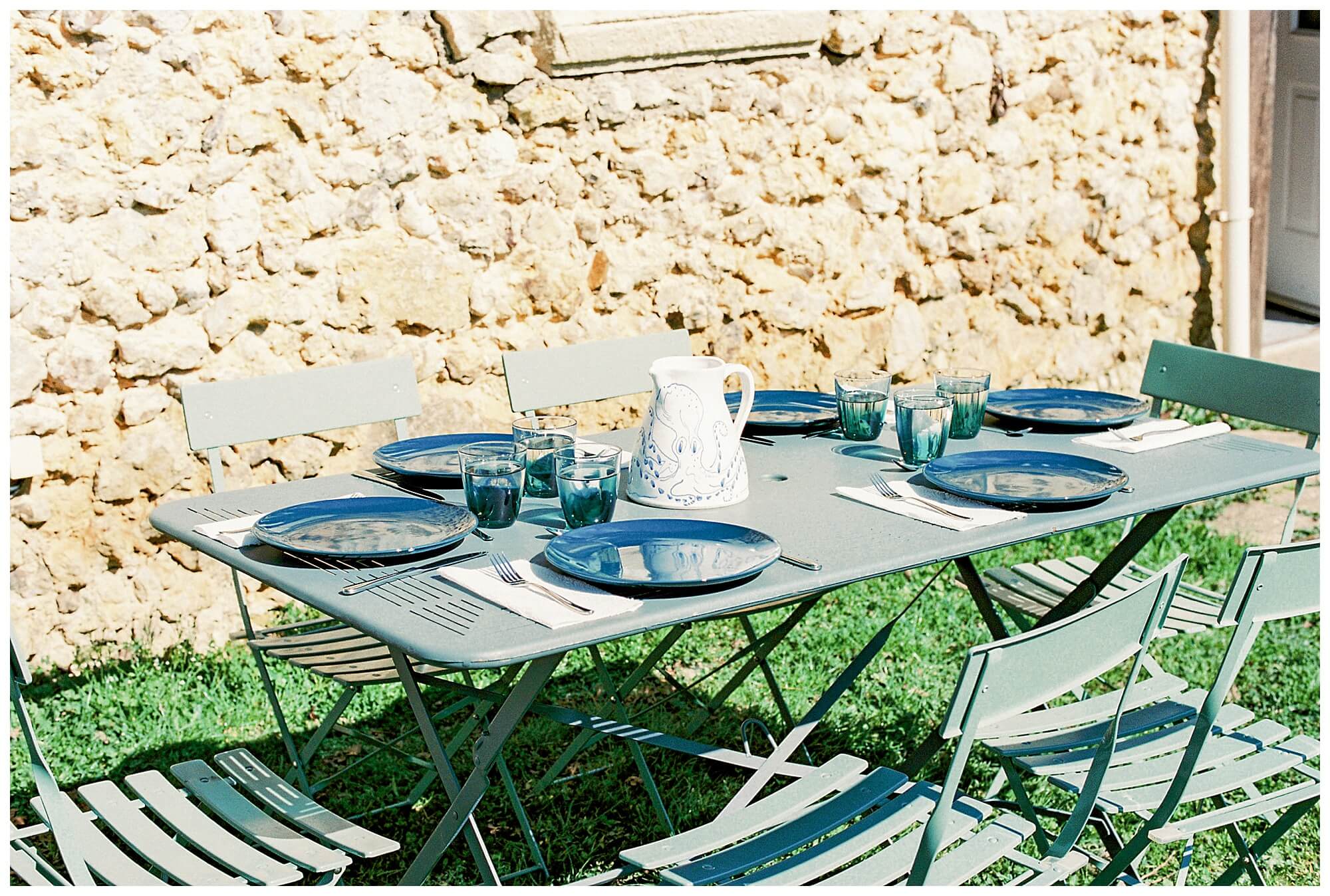Full sun shines on the stone French country cottage and the garden table set for lunch.