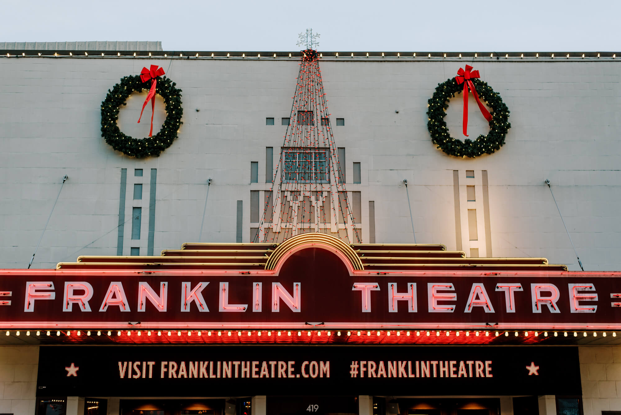 the franklin theatre in franklin, tennessee glows at sunset. there are two christmas wreaths hanging from the roof.