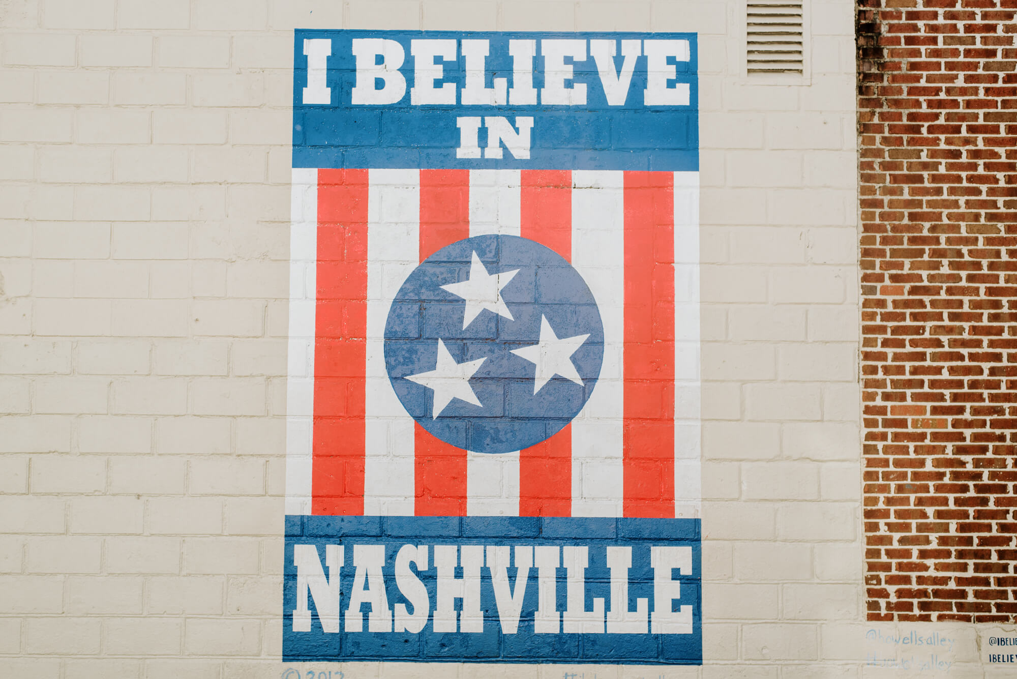 a vertical, rectangular mural painted on a white brick wall in Nashville's 12 South neighborhood. The mural is red, white, and blue with stripes and stars. It says "I believe in Nashville."