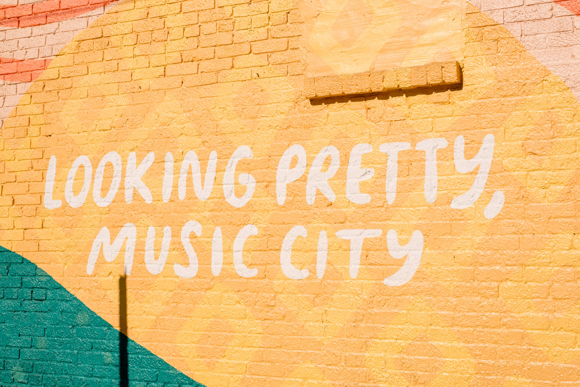 up-close photo of an orange, yellow, and green painted brick wall in Nashville's 12 South neighborhood. White hand-written text reads "Looking pretty, Music City."